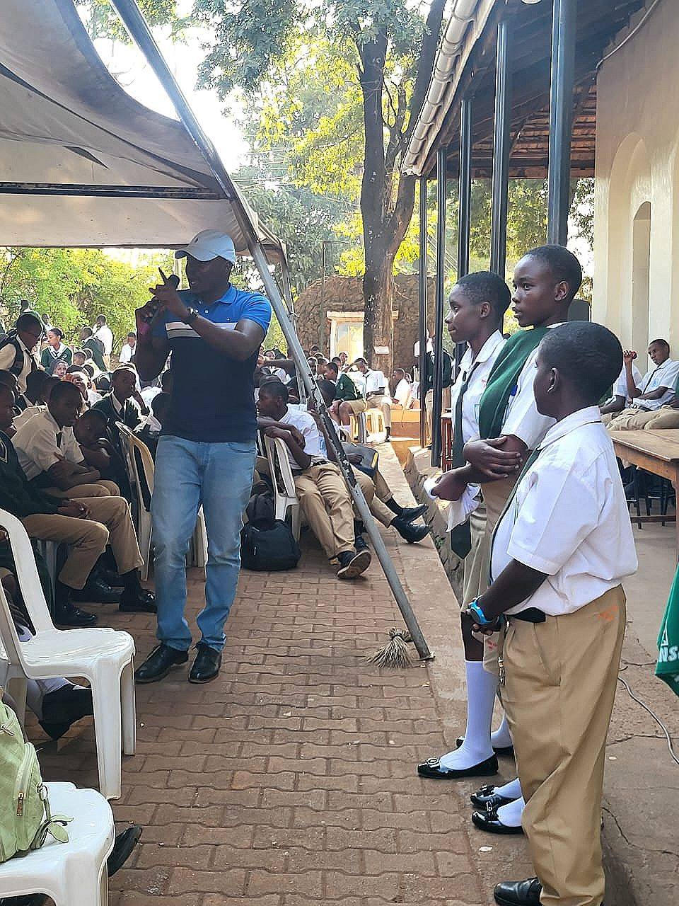 A speaker with a microphone beside student leaders at an outdoor school assembly