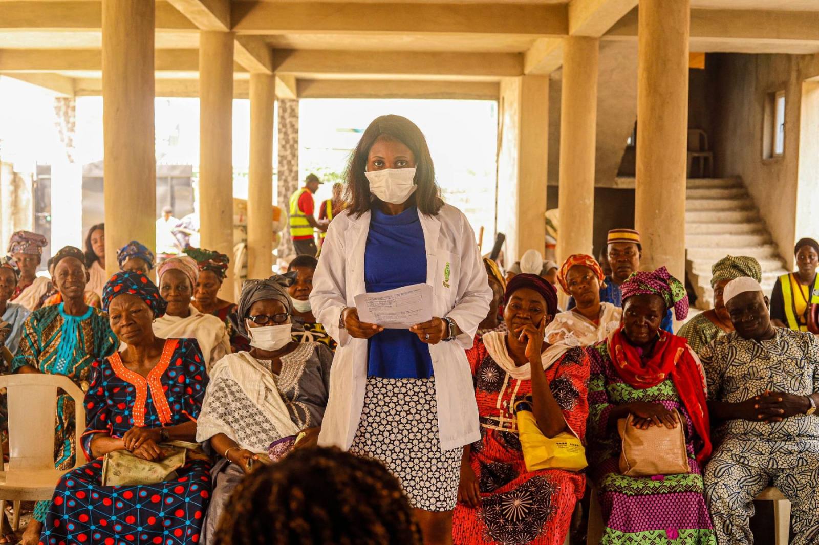 A health worker speaking to a seated group of women in the community