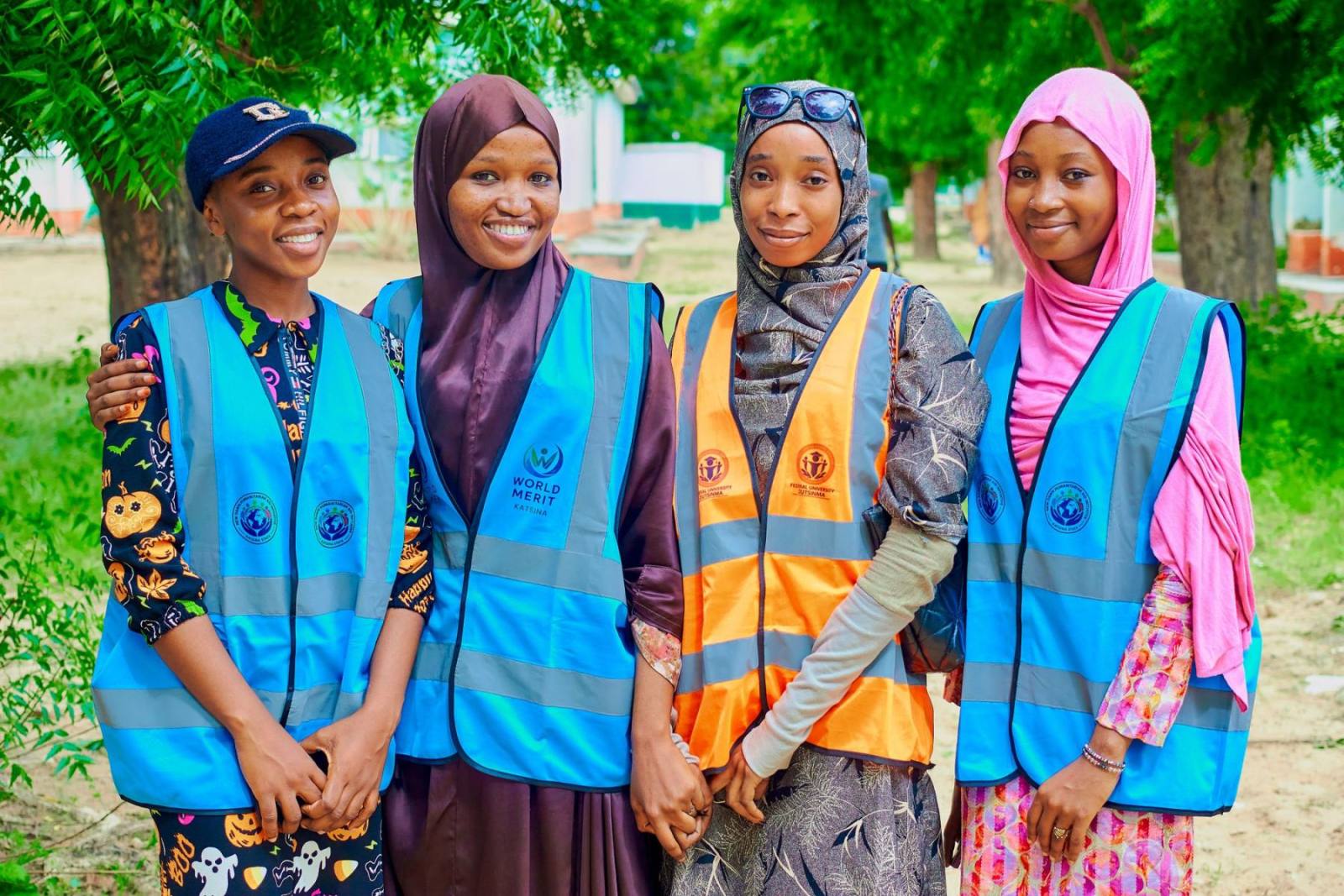 Four young volunteers in high-visibility vests smiling outdoors